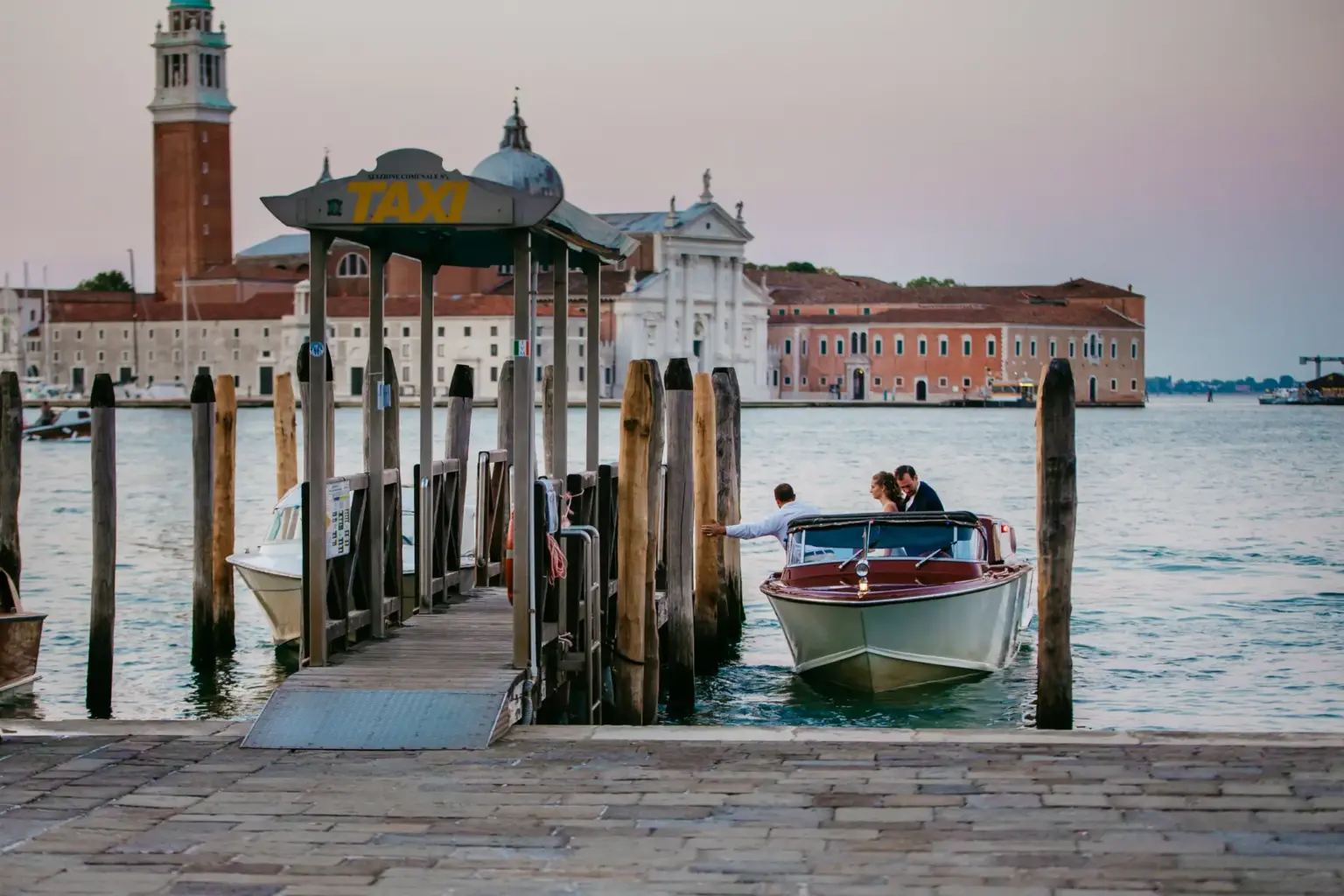 Klassisches venezianisches Wassertaxi aus Holz fährt bei Sonnenaufgang über die ruhige Lagune – ein typischer, luxuriöser Moment einer Hochzeitsreise in Italien.