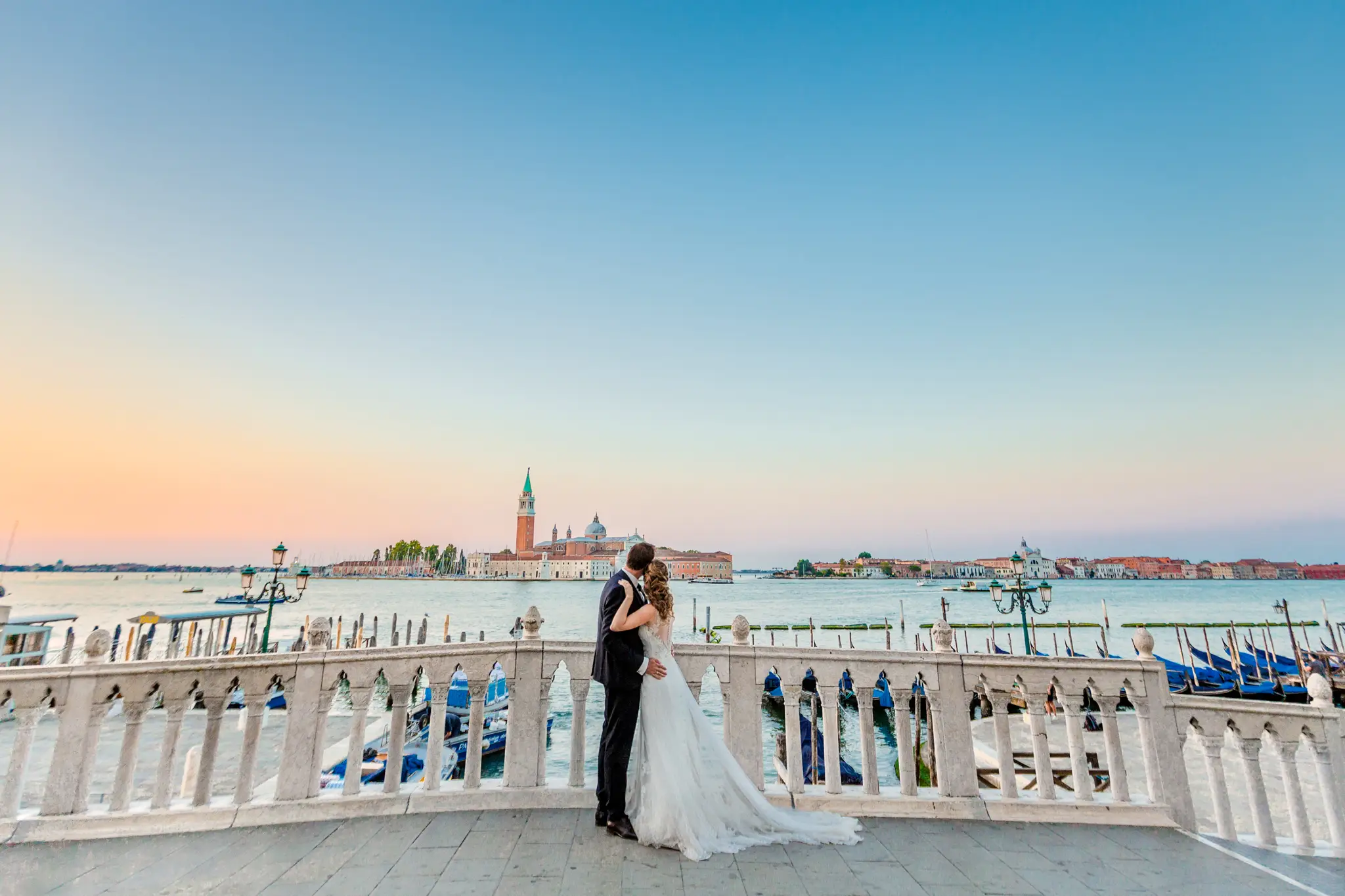 HOCHZEITSFOTOGRAF VENEDIG 39 Brautpaar genießt bei einem exklusiven Destination Wedding Shooting in Venedig den weiten Ausblick über die Lagune auf die Insel San Giorgio Maggiore im pastellfarbenen Morgenlicht.