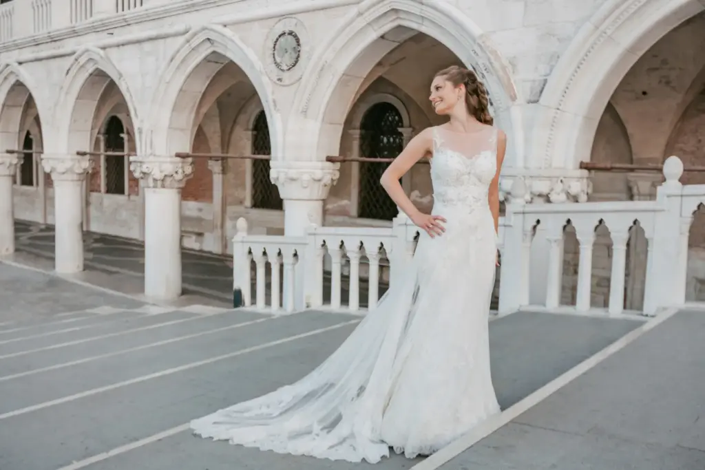 Elegante Braut präsentiert ihr fließendes Hochzeitskleid mit langer Schleppe auf einem hölzernen Bootssteg im warmen Morgenlicht von Venedig