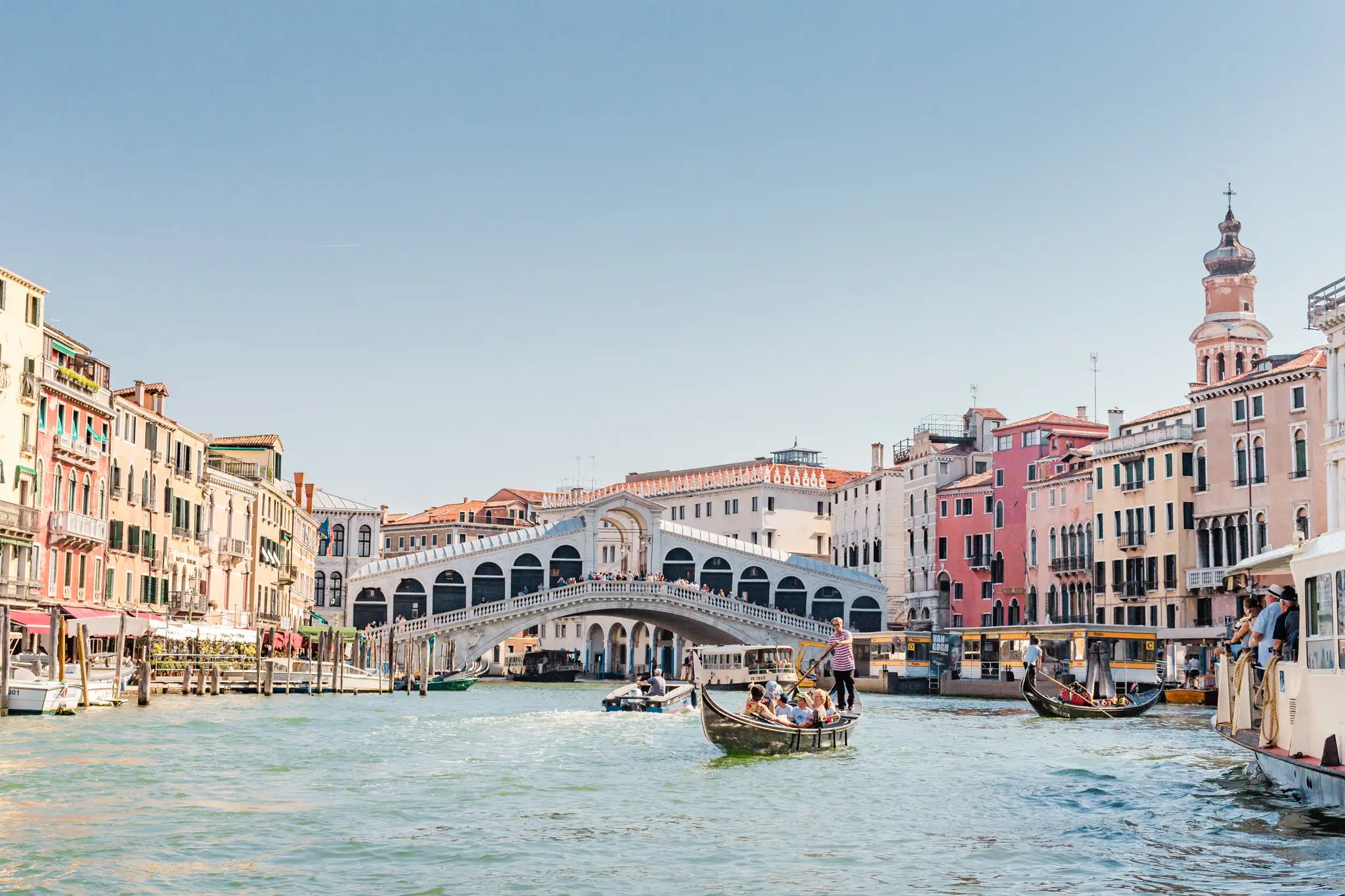 HOCHZEITSFOTOGRAF VENEDIG 57 Klassischer Blick auf den Canal Grande mit der Rialtobrücke, Gondeln und Vaporetti im sommerlichen Mittagslicht. Die Kulisse für Hochzeitsfotos in Venedig.
